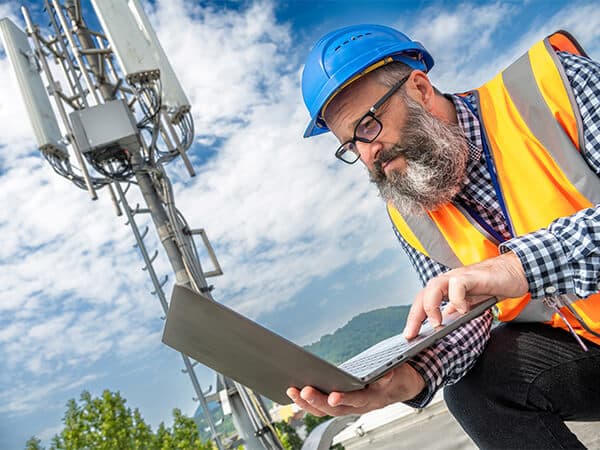 Wholesale Backhaul Feature Tile 600x450 Cell tower worker looking at laptop with cell tower in background